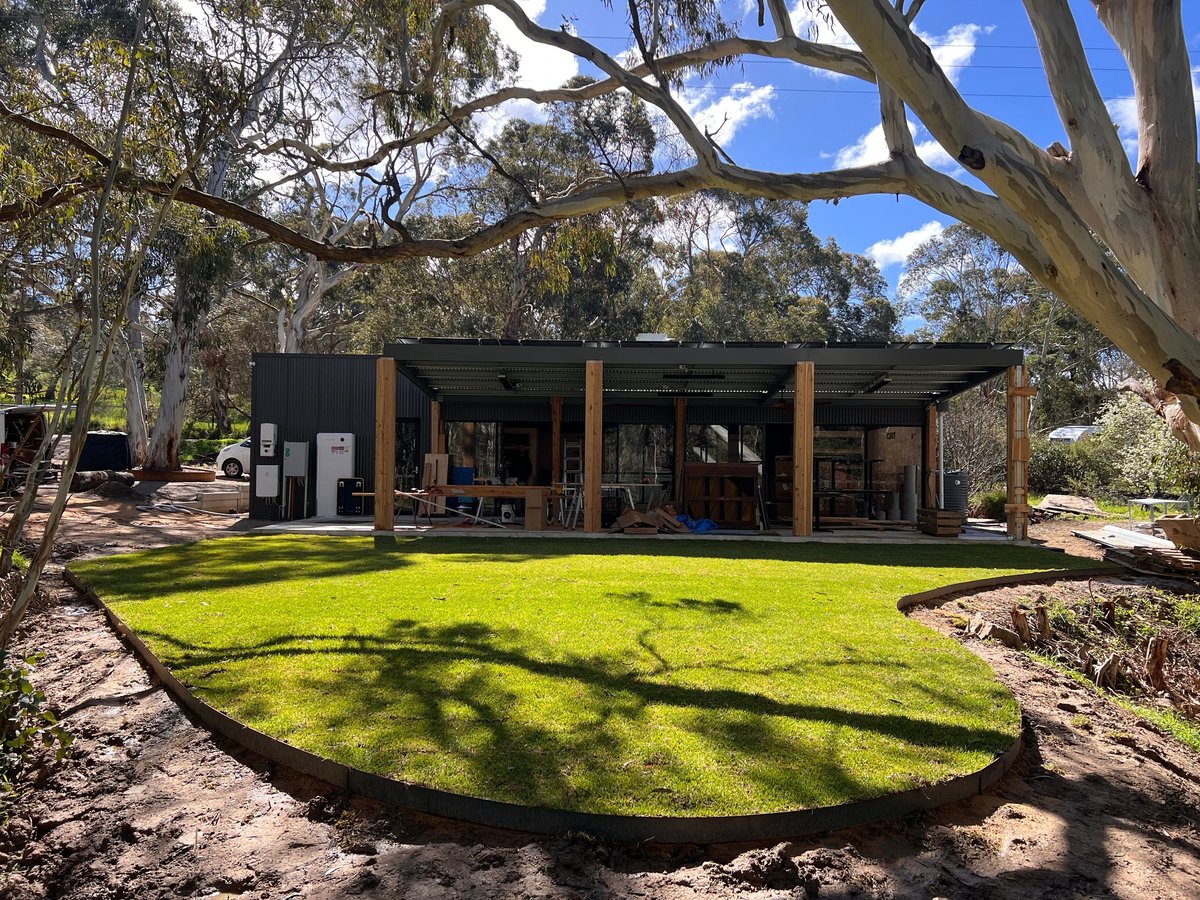 Modern black building with wooden posts nestled under large eucalyptus trees, surrounded by green lawn and natural landscape