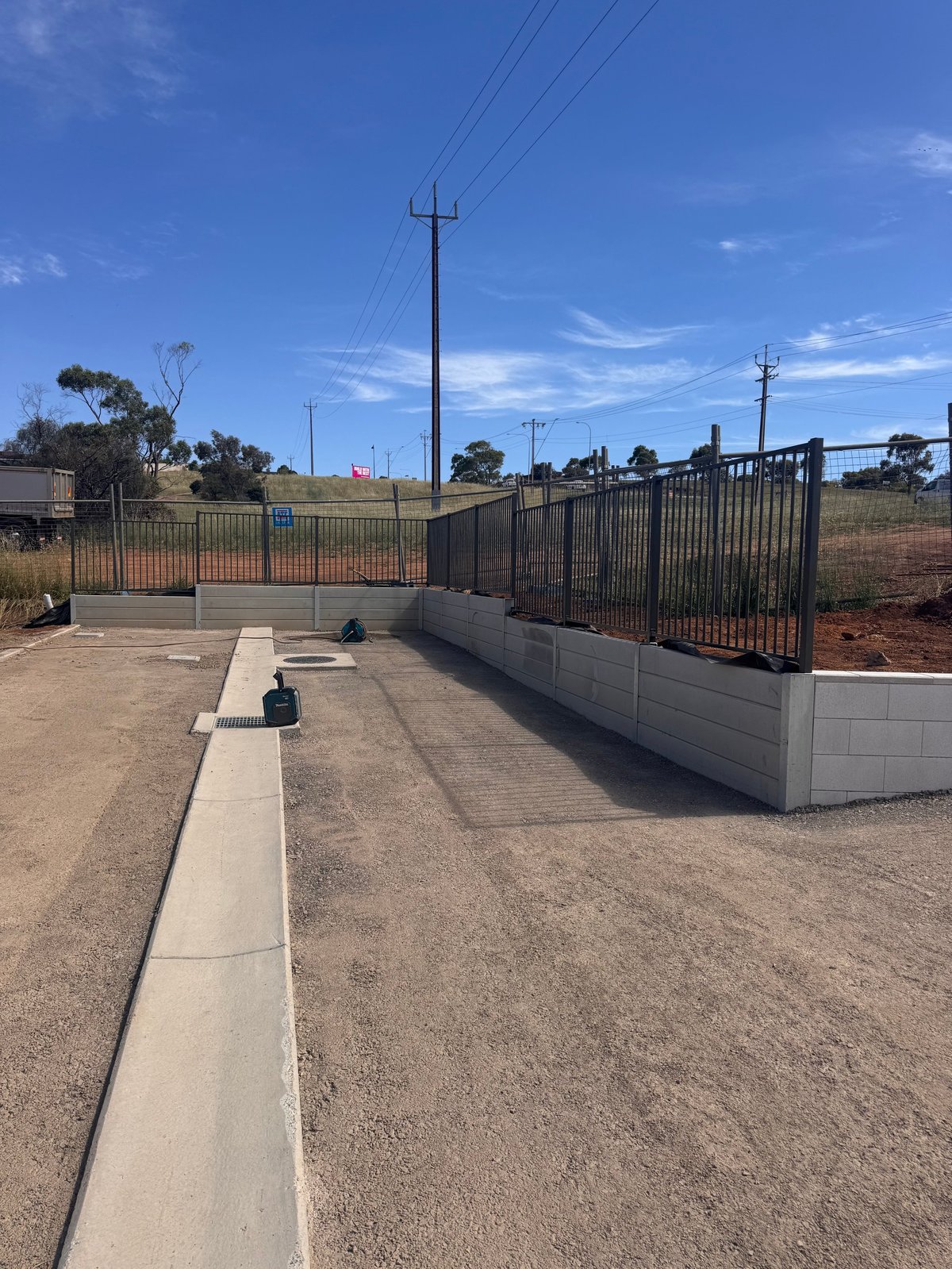 Concrete driveway with black metal gate and white brick fence under clear blue sky with power lines visible
