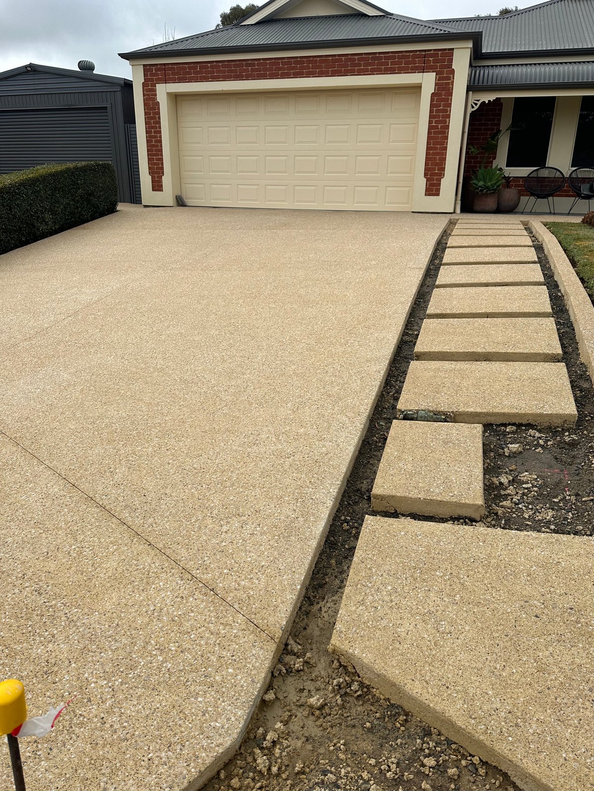 Modern brick home with large cream-colored concrete driveway, cream stepping stones, and cream garage door with black trim