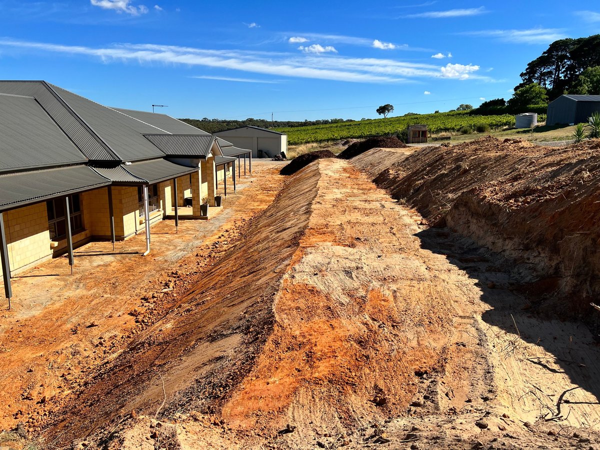 New rural construction site with modern house, earthwork trenches, and cleared farmland under blue sky