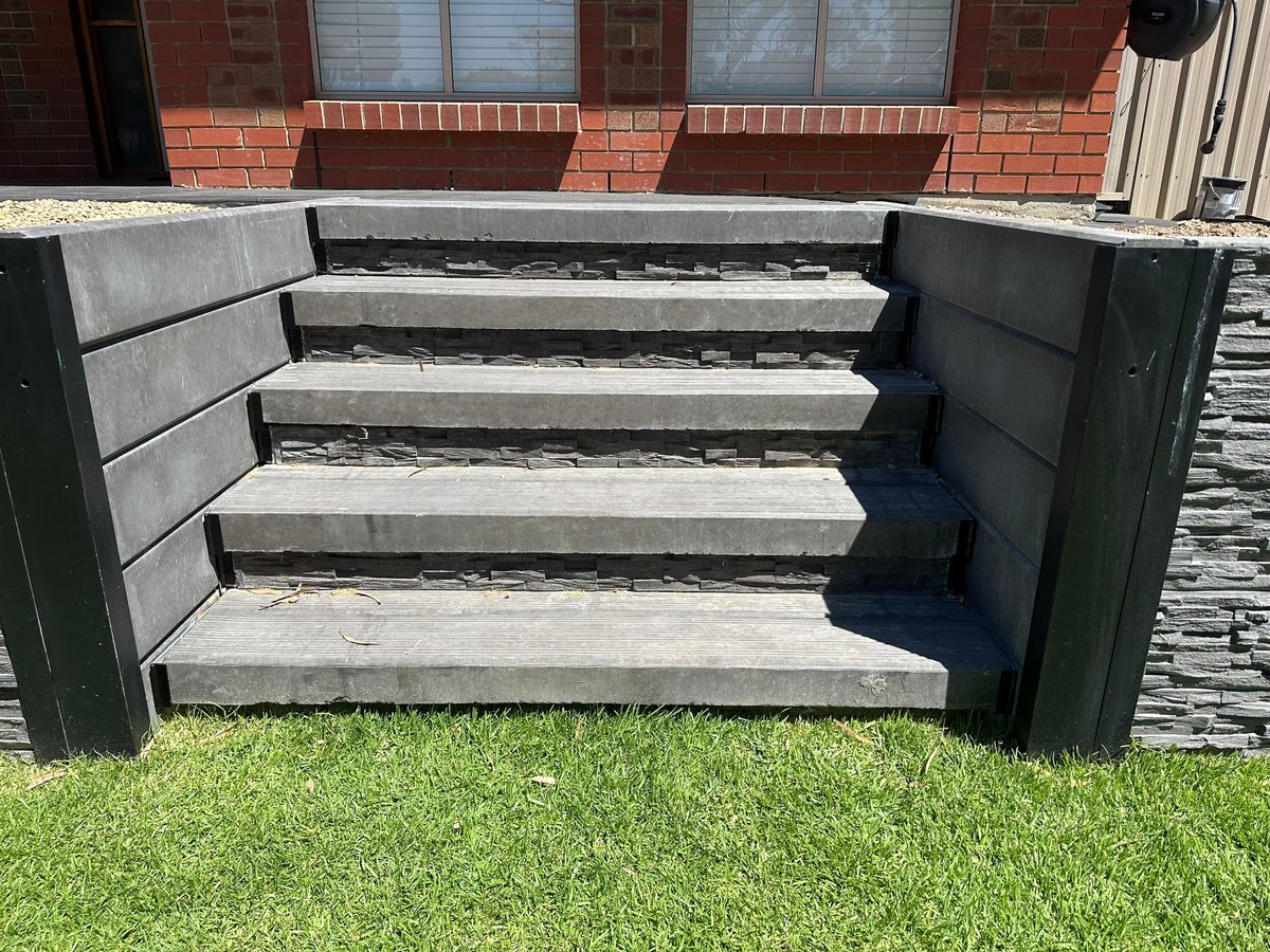 Concrete outdoor steps with black metal railings, set on green grass against a brick building