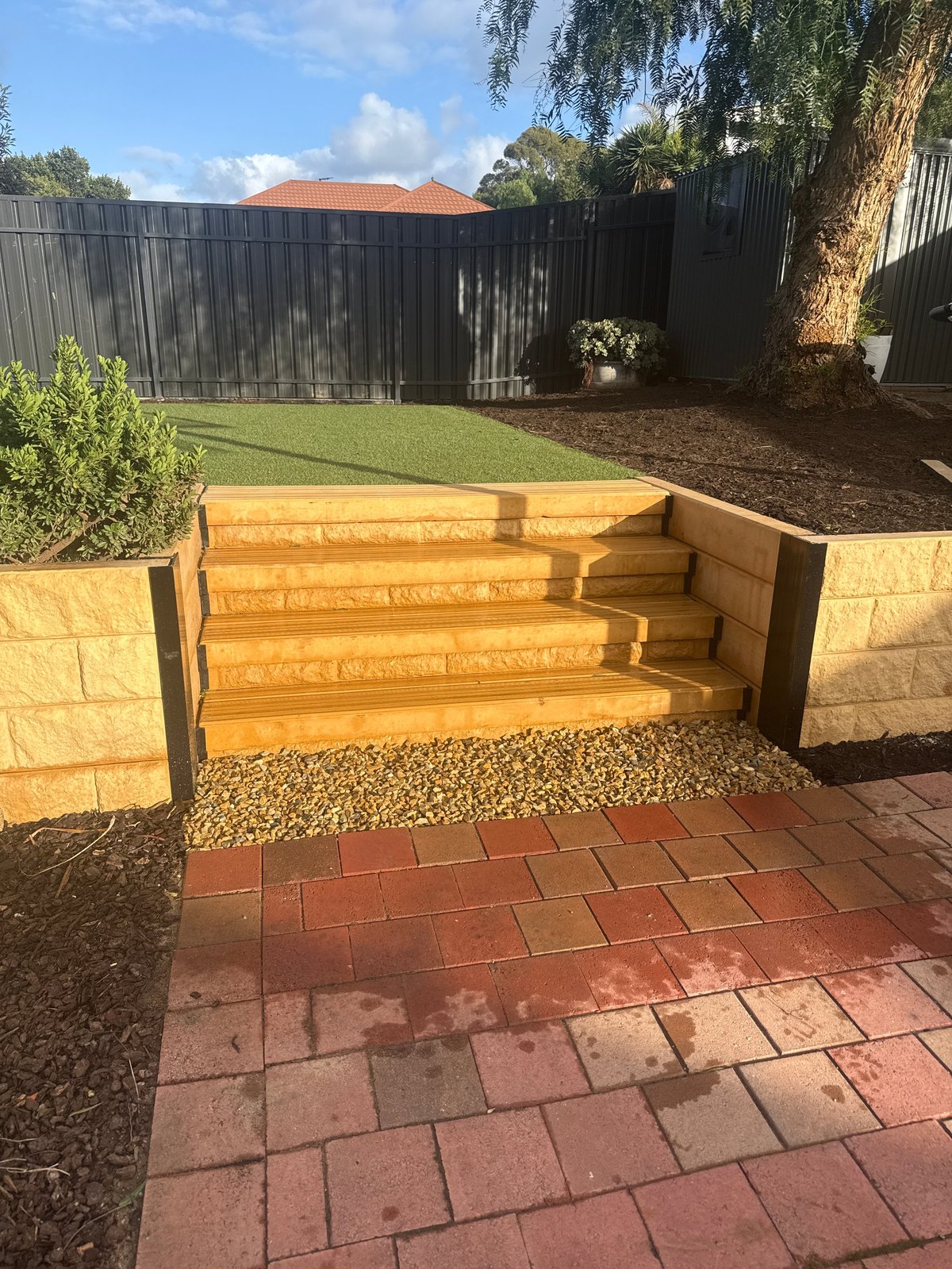 Wooden garden steps with stone walls in a landscaped backyard with red brick patio and green lawn