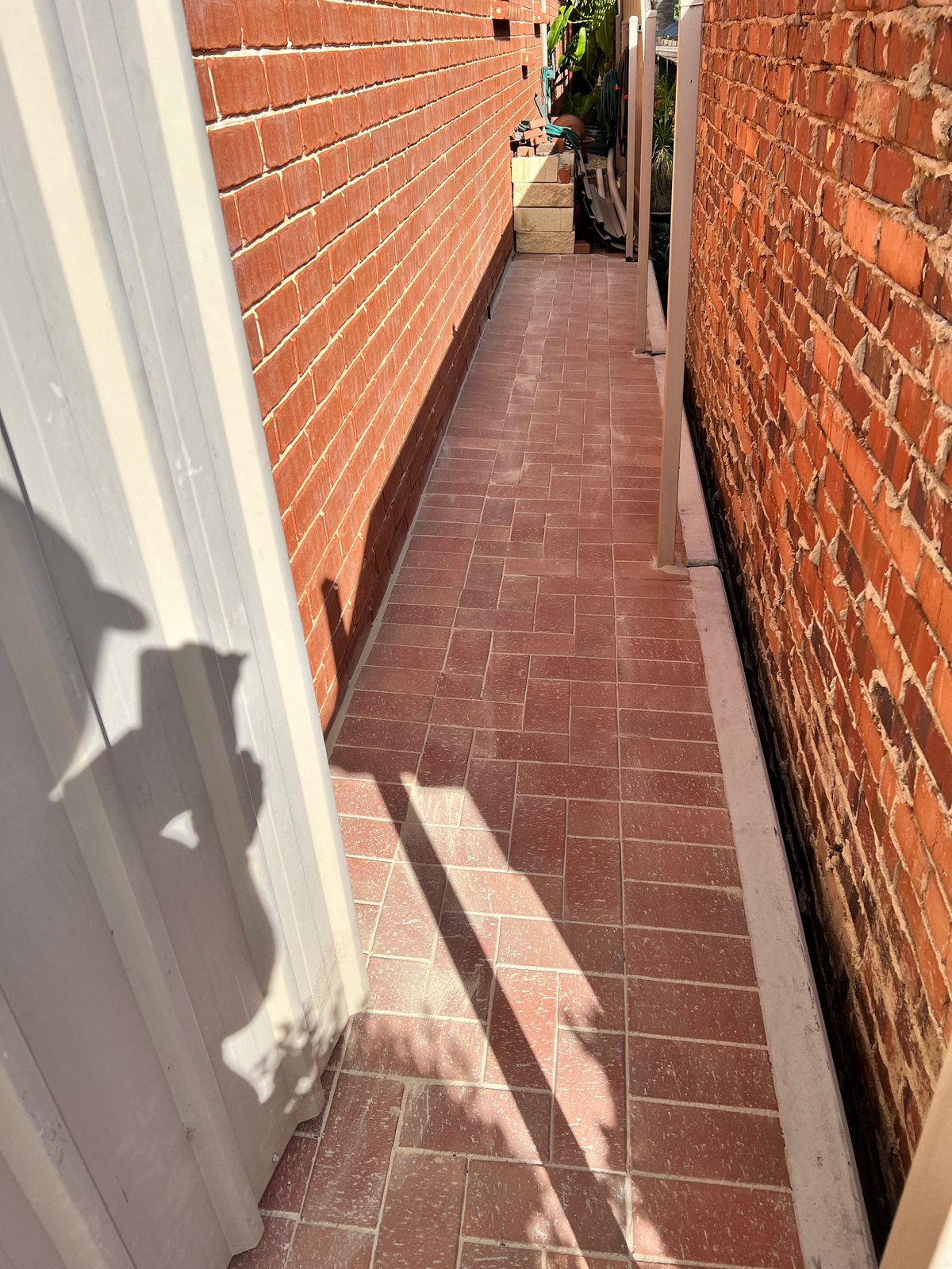 Narrow brick passageway between two red brick buildings with white trim on the left side and terracotta tile flooring