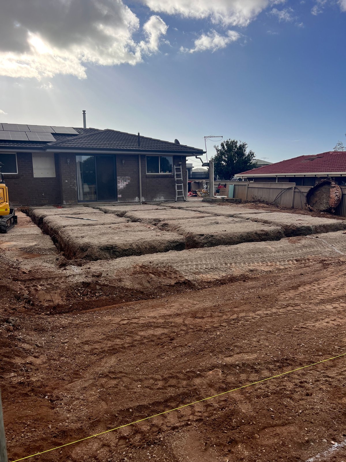 Construction site with brown soil, fabric drainage, and residential houses with black and red roofs under blue sky