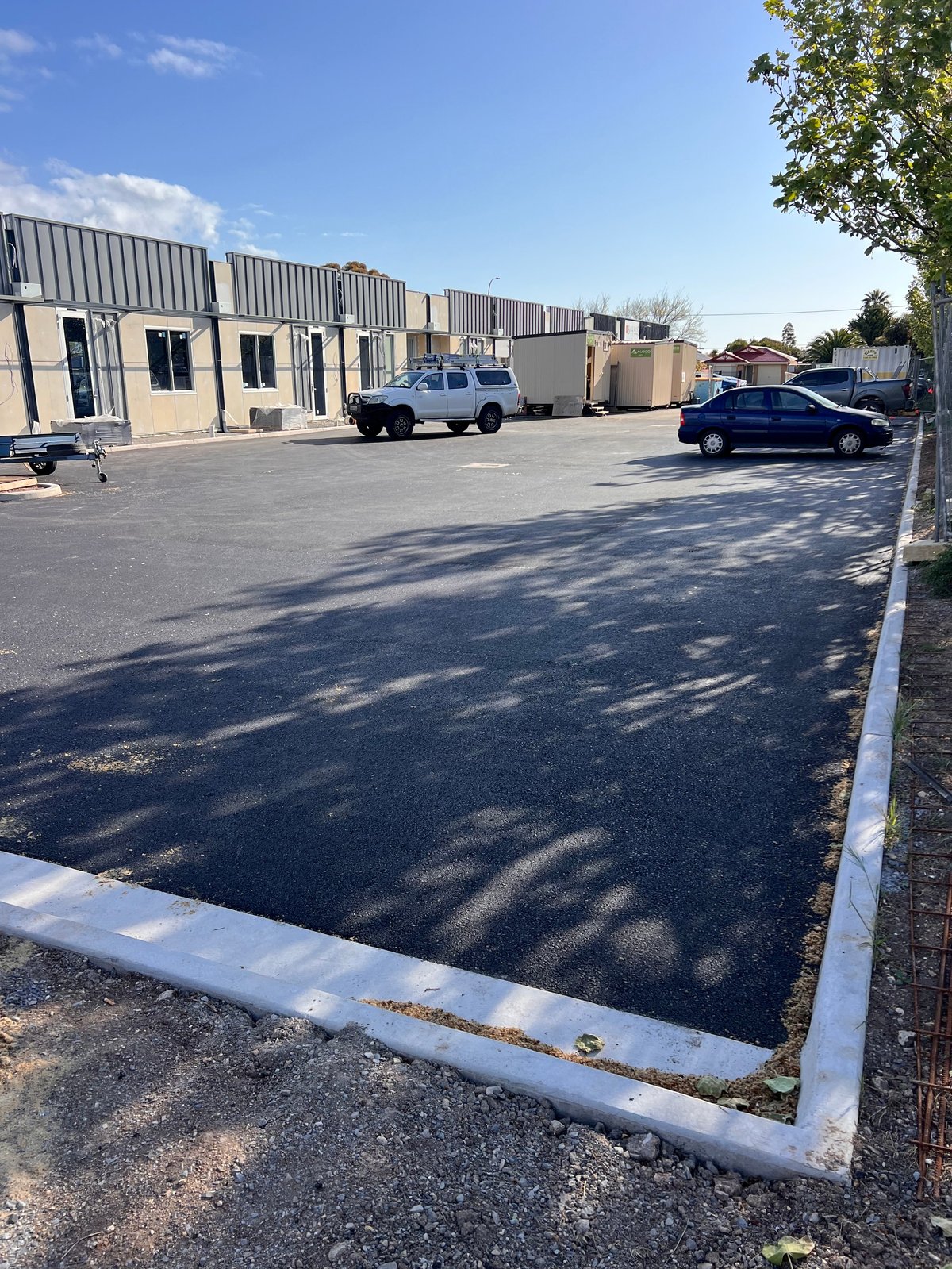 Commercial parking lot with industrial building, parked vehicles, and white boundary markings on asphalt