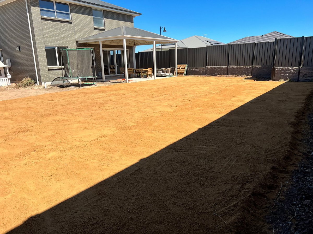 New residential home with patio area and half-finished landscaping showing exposed brown dirt yard under clear blue sky