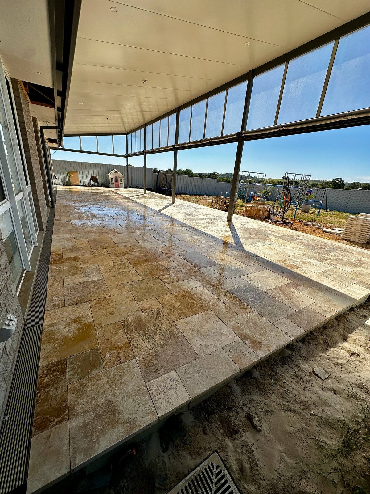 Large covered patio with tile flooring, floor-to-ceiling windows overlooking rural landscape with fencing and green fields