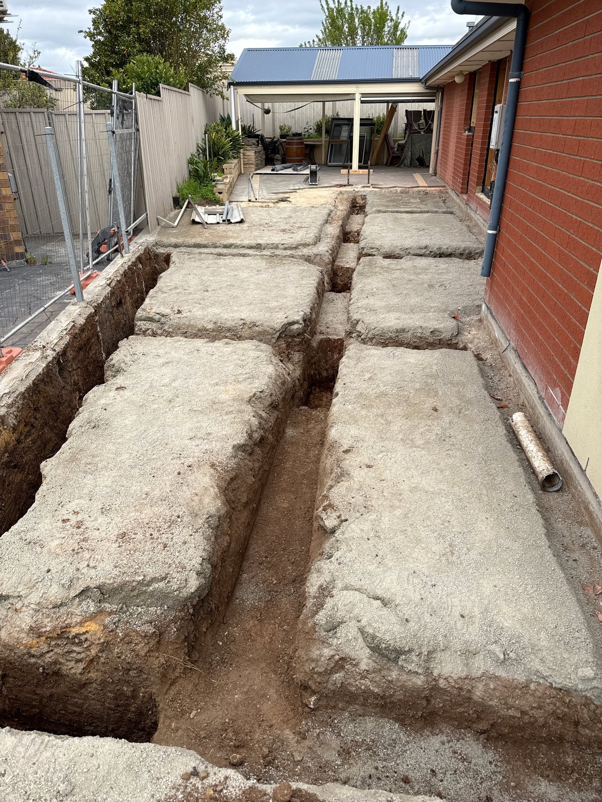 Backyard construction site with trenches dug in concrete ground next to red brick house