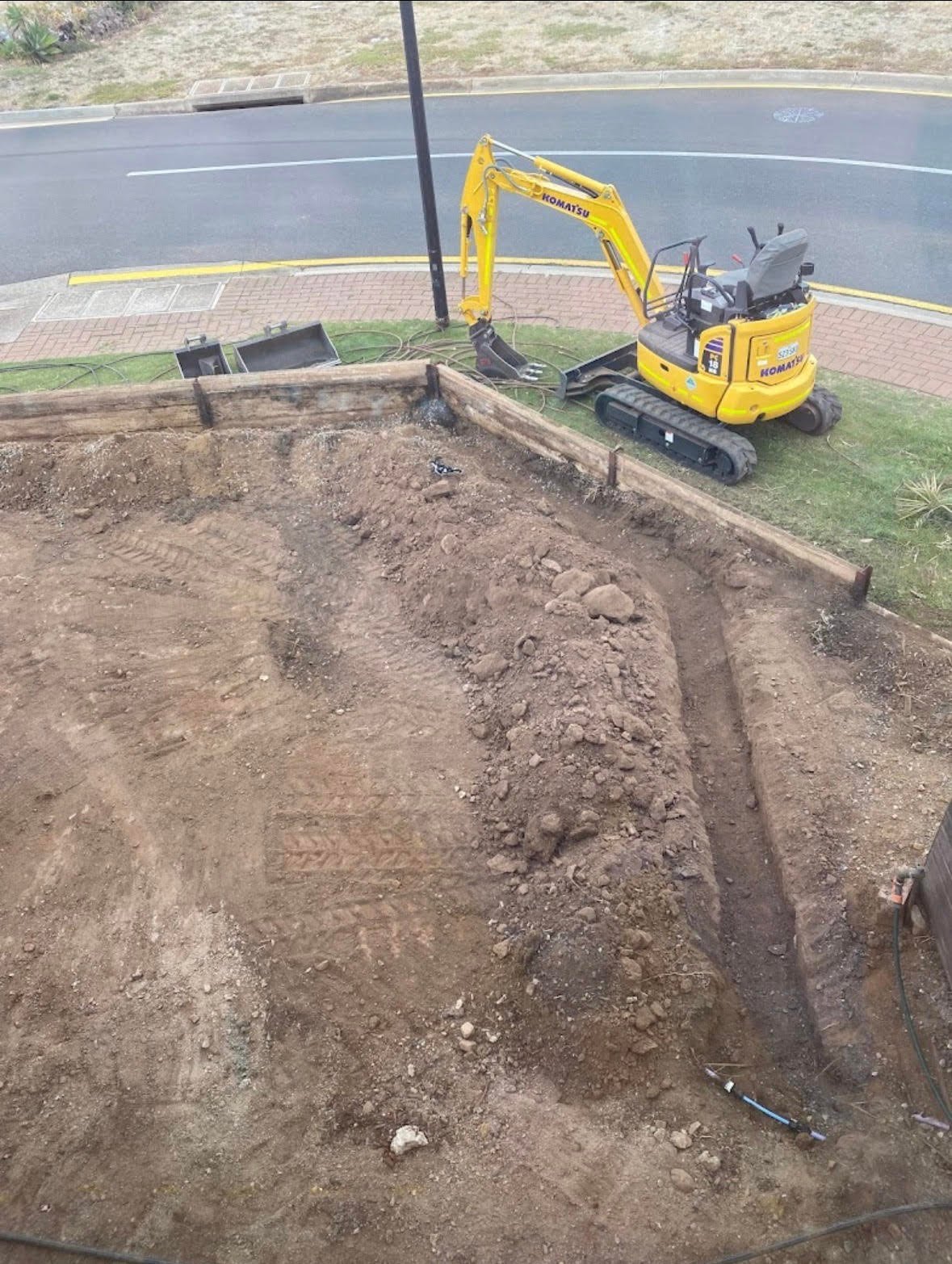 Yellow mini excavator digging in a soil trench next to a paved road and utility pole