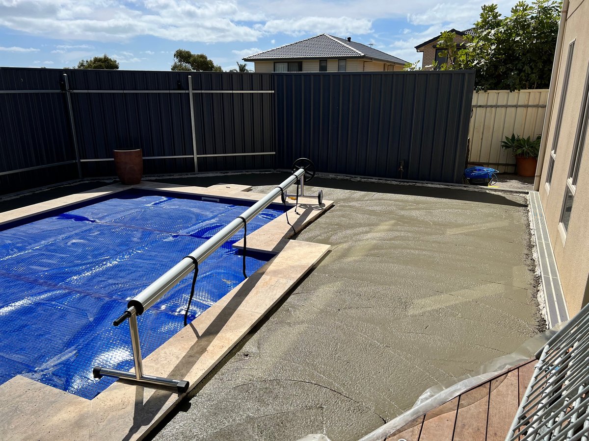 Backyard with covered swimming pool, concrete patio, and black metal fence surrounded by residential houses