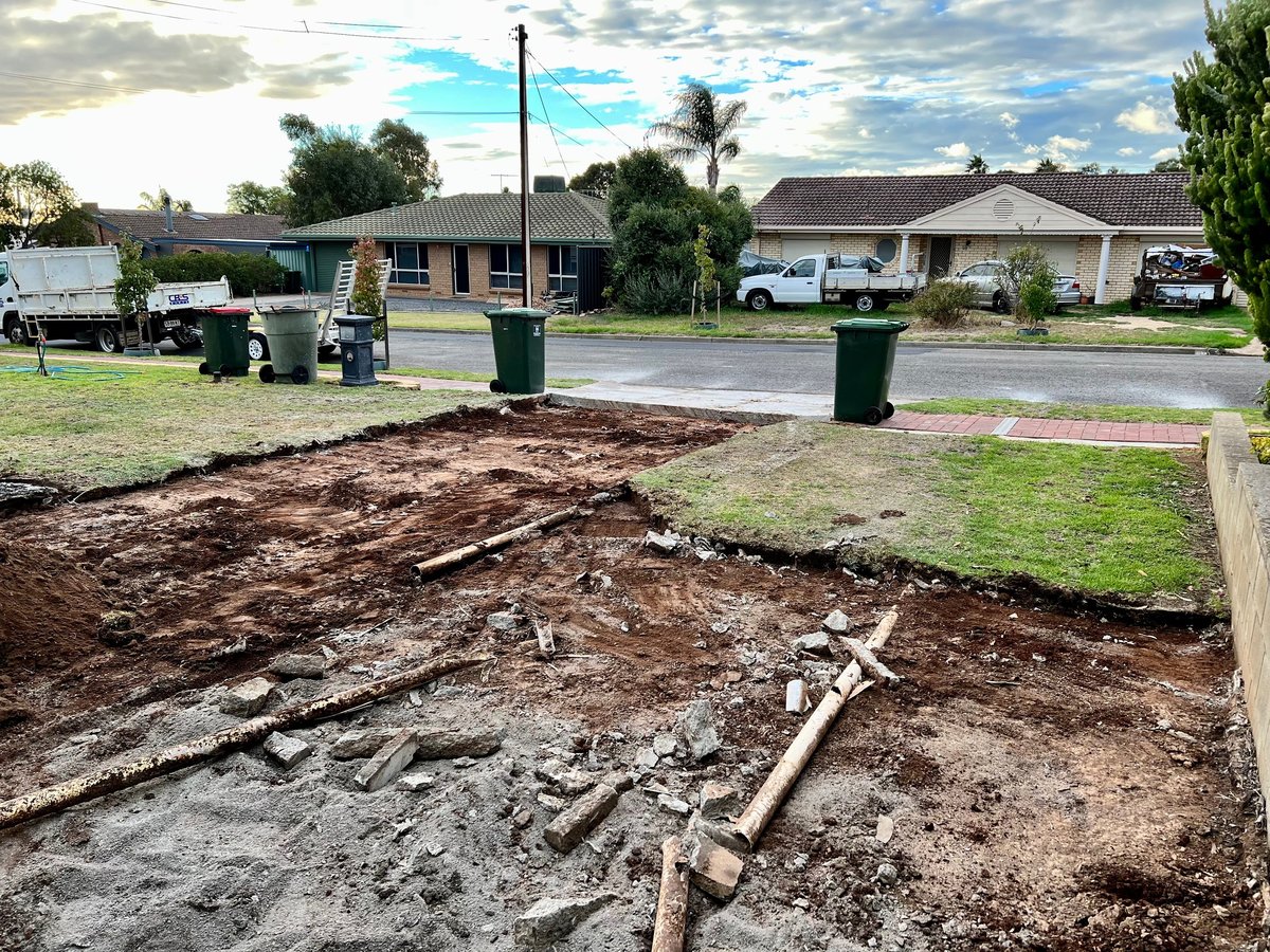 Residential yard with exposed soil, exposed pipes, and trash cans, suburban neighborhood with houses and palm trees